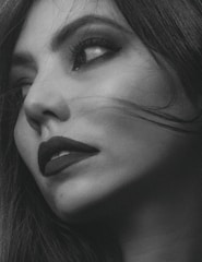 Close-up black and white photo of a model's face with sharp shadows highlighting elegant makeup.