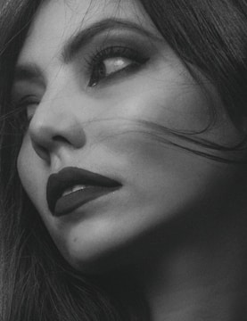 Close-up black and white photo of a model's face with sharp shadows highlighting elegant makeup.