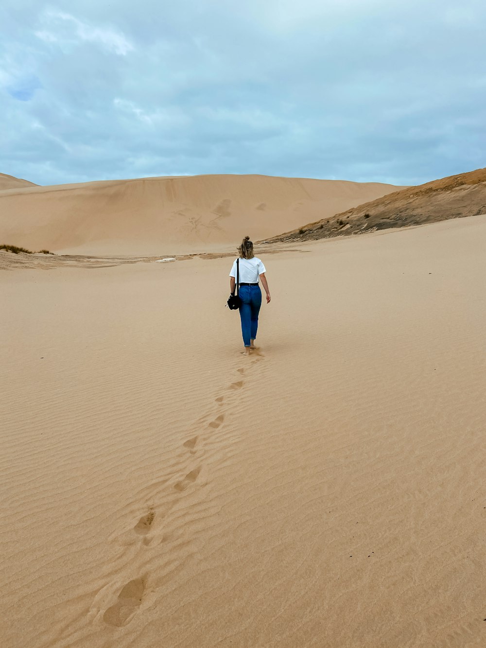 woman in white jacket walking on brown sand during daytime