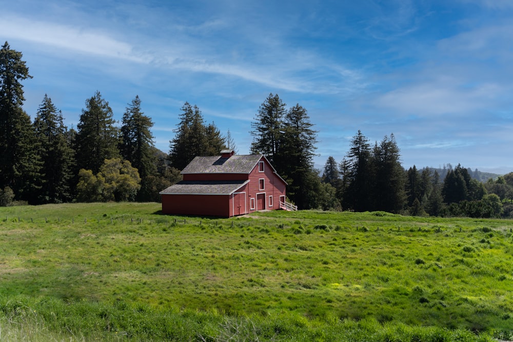 red wooden house on green grass field near green trees under blue sky during daytime