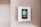 A digital thermostat is mounted on a beige wall. The thermostat has an LED screen displaying the temperature settings and controls below it. The overall look is clean and minimalistic.