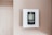 A digital thermostat is mounted on a beige wall. The thermostat has an LED screen displaying the temperature settings and controls below it. The overall look is clean and minimalistic.