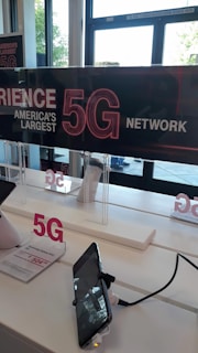 A display inside a store features signage promoting America's largest 5G network. Two smartphones are mounted on stands, one with a visible price tag offering a Samsung Galaxy A32 for $504.00. The background shows clear glass doors and windows, providing natural light to the interior.
