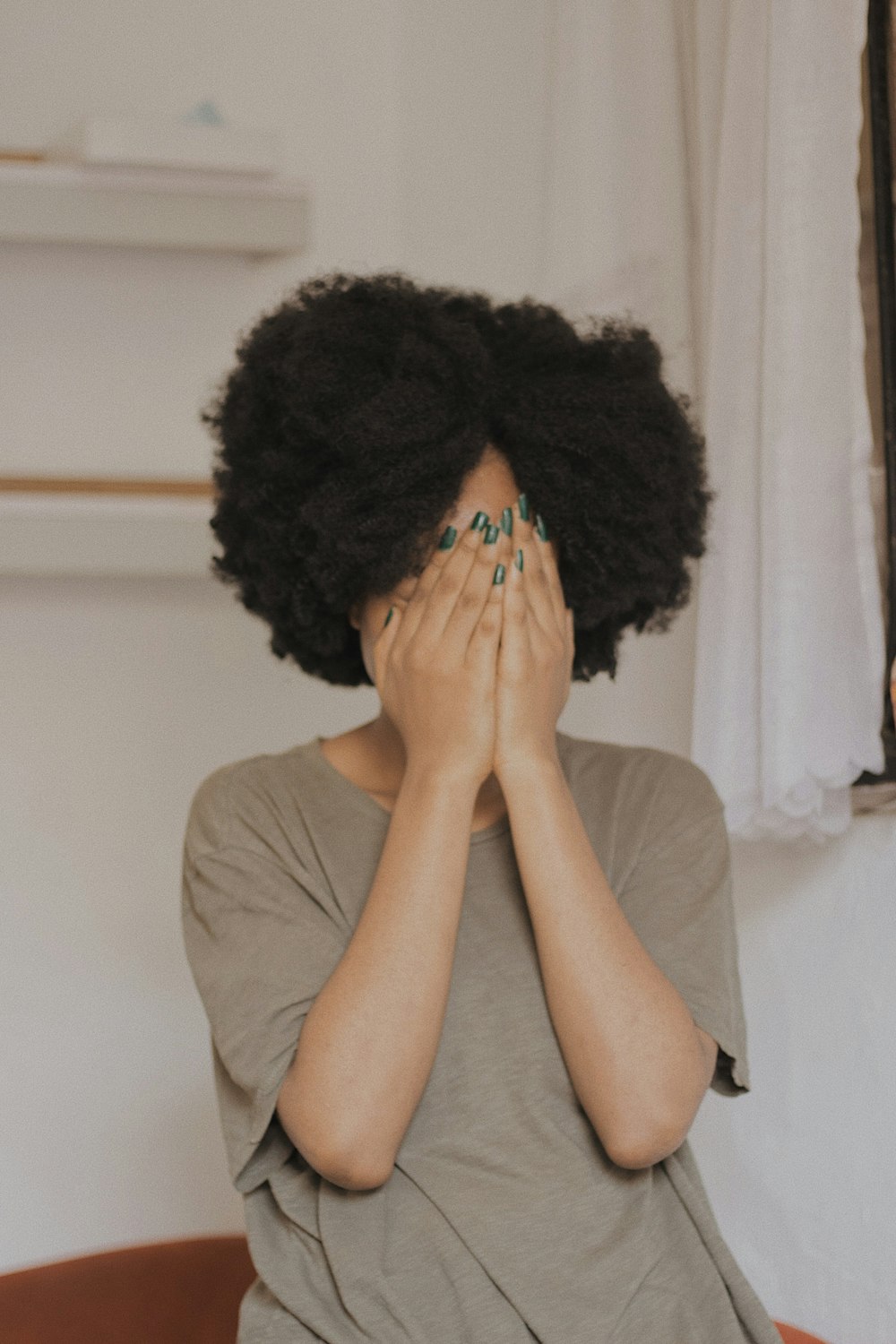 woman in gray t-shirt covering face with both hands