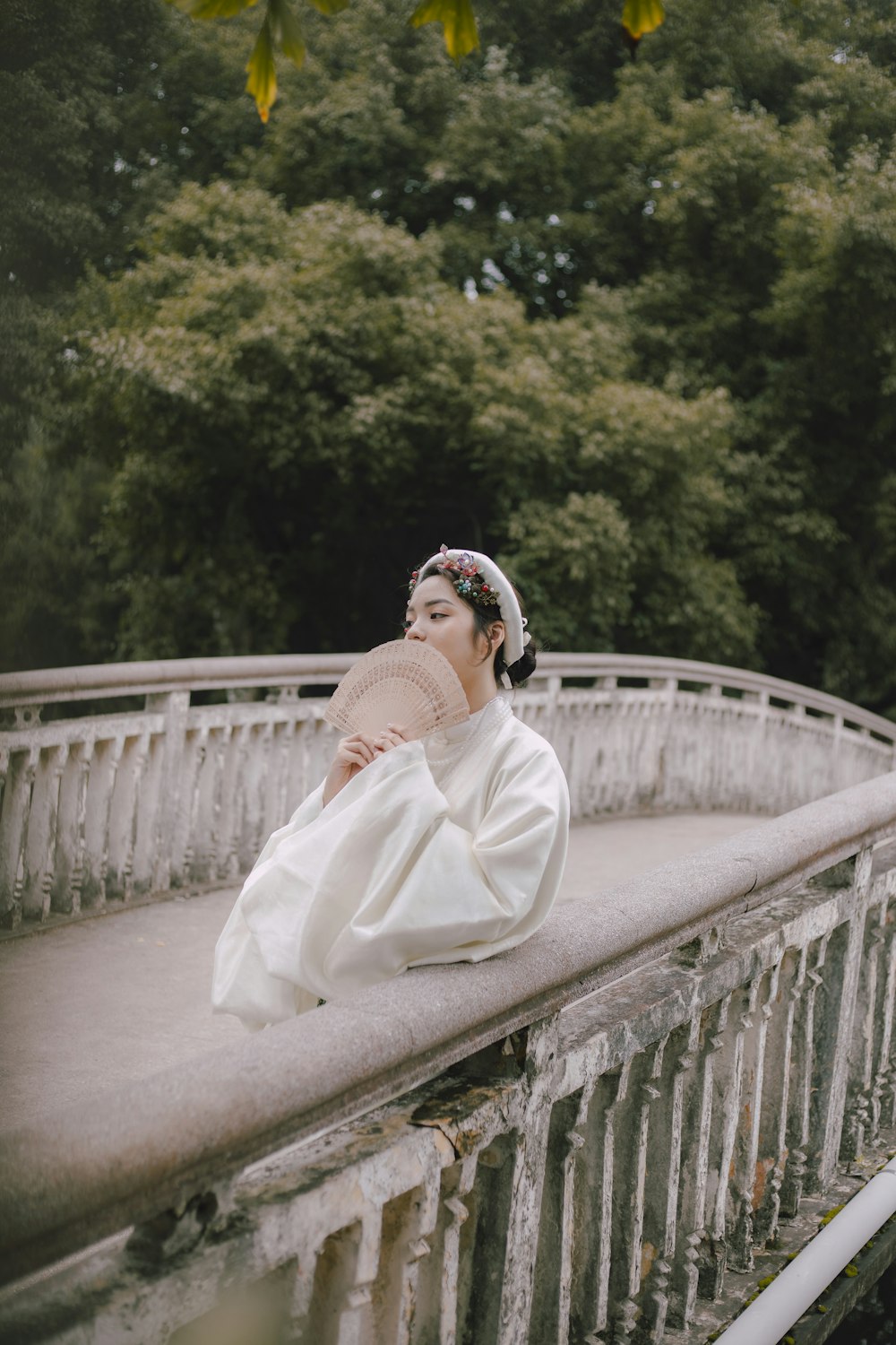 woman in white robe sitting on white concrete bridge during daytime