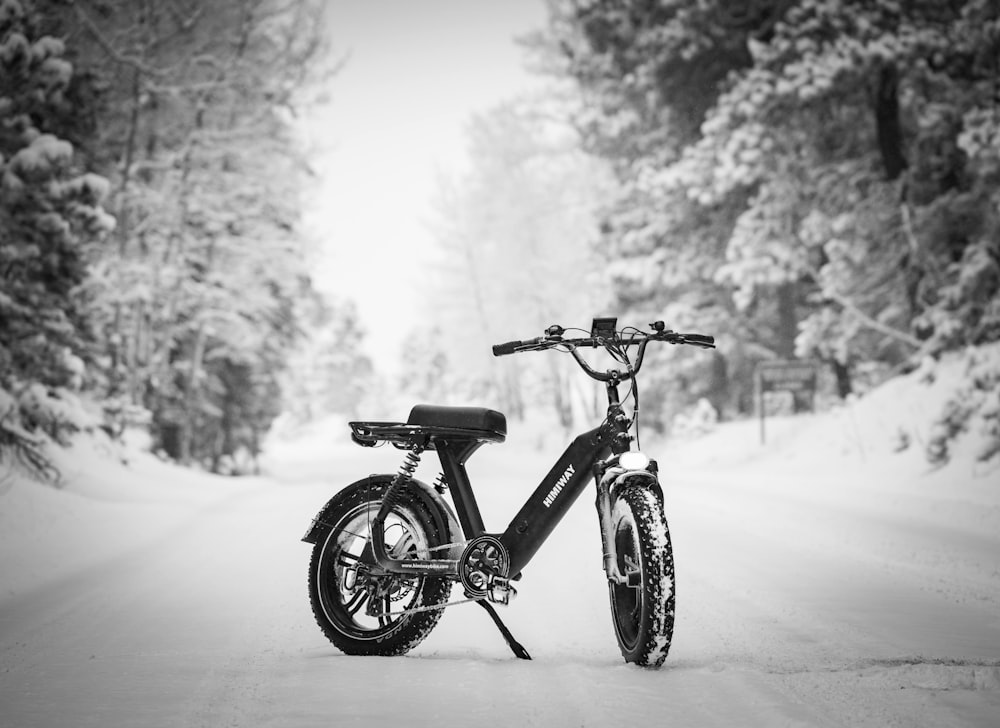 foto em tons de cinza da bicicleta preta no chão coberto de neve