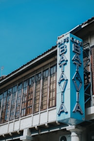 A vintage-style building with large, rectangular windows featuring a vertical sign reading 'Cafe Batavia' in blue neon letters. The architectural design includes a tiled roof and wooden window frames.