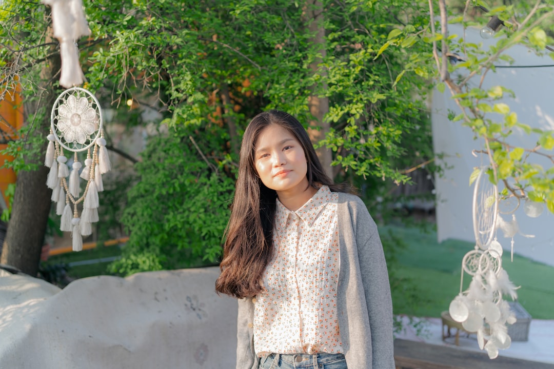 woman in gray cardigan standing near green trees during daytime