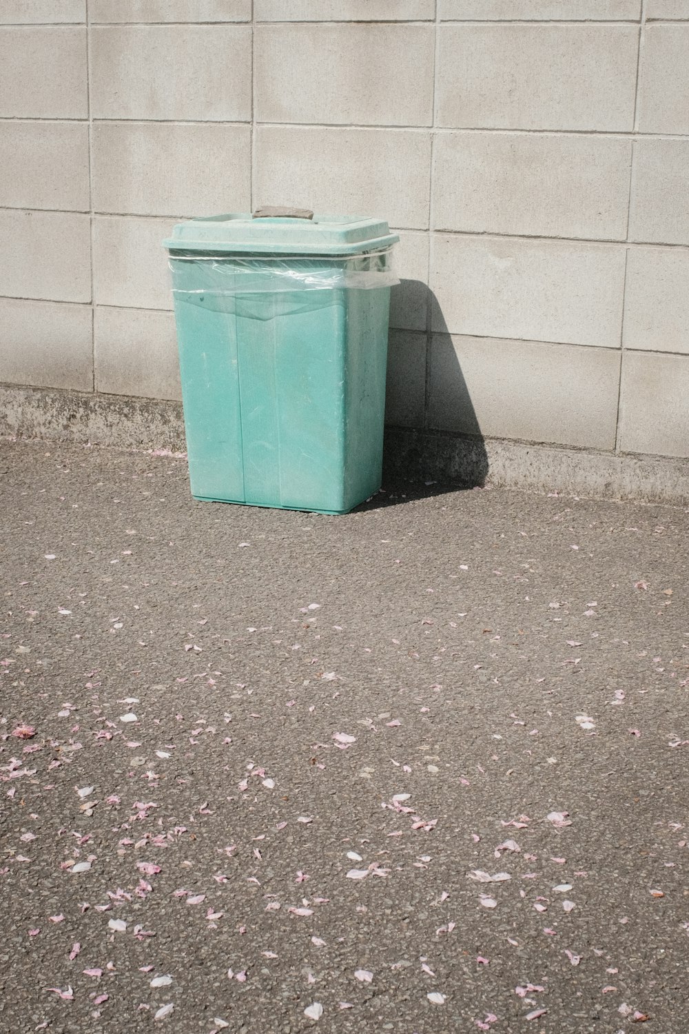 白い壁の横の緑色のプラスチック製のゴミ箱