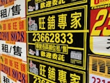 A collection of colorful advertisement posters displayed on a wall, featuring large, bold text in various fonts, primarily in Chinese characters, with some English text. Yellow, black, and red are the prominent color schemes used in the posters.