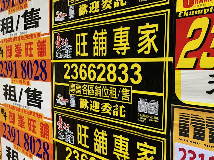 A collection of colorful advertisement posters displayed on a wall, featuring large, bold text in various fonts, primarily in Chinese characters, with some English text. Yellow, black, and red are the prominent color schemes used in the posters.