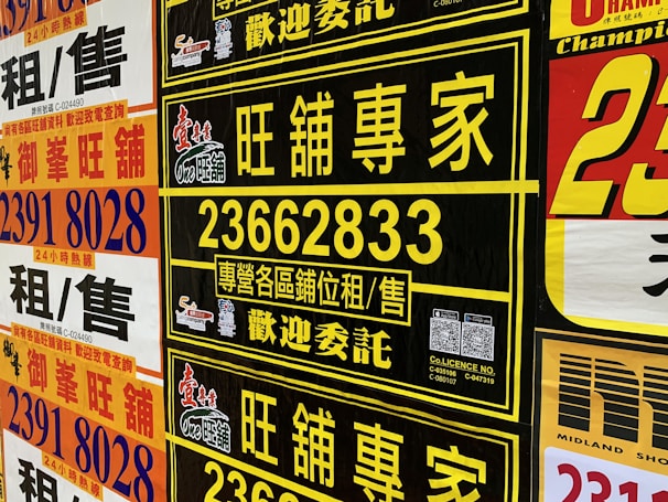 A collection of colorful advertisement posters displayed on a wall, featuring large, bold text in various fonts, primarily in Chinese characters, with some English text. Yellow, black, and red are the prominent color schemes used in the posters.