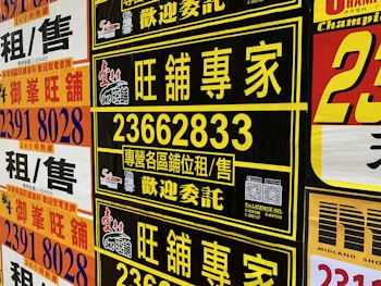 A collection of colorful advertisement posters displayed on a wall, featuring large, bold text in various fonts, primarily in Chinese characters, with some English text. Yellow, black, and red are the prominent color schemes used in the posters.
