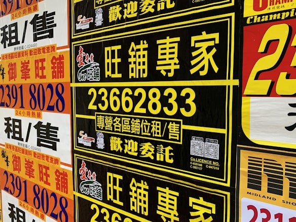 A collection of colorful advertisement posters displayed on a wall, featuring large, bold text in various fonts, primarily in Chinese characters, with some English text. Yellow, black, and red are the prominent color schemes used in the posters.