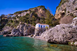 white and brown concrete building on rocky mountain beside body of water during daytime