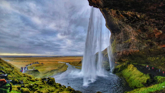 Seljalandsfoss waterfall seen from behind the rock ledge, with visitors on the path below.