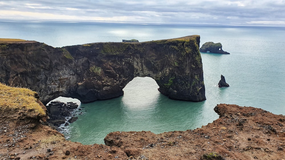 green and brown rock formation on sea under white clouds during daytime