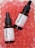 Two bottles of face serum with vitamin C are positioned on a surface filled with pink translucent gel-like beads. The bottles have black droppers and white labels with red and black text.