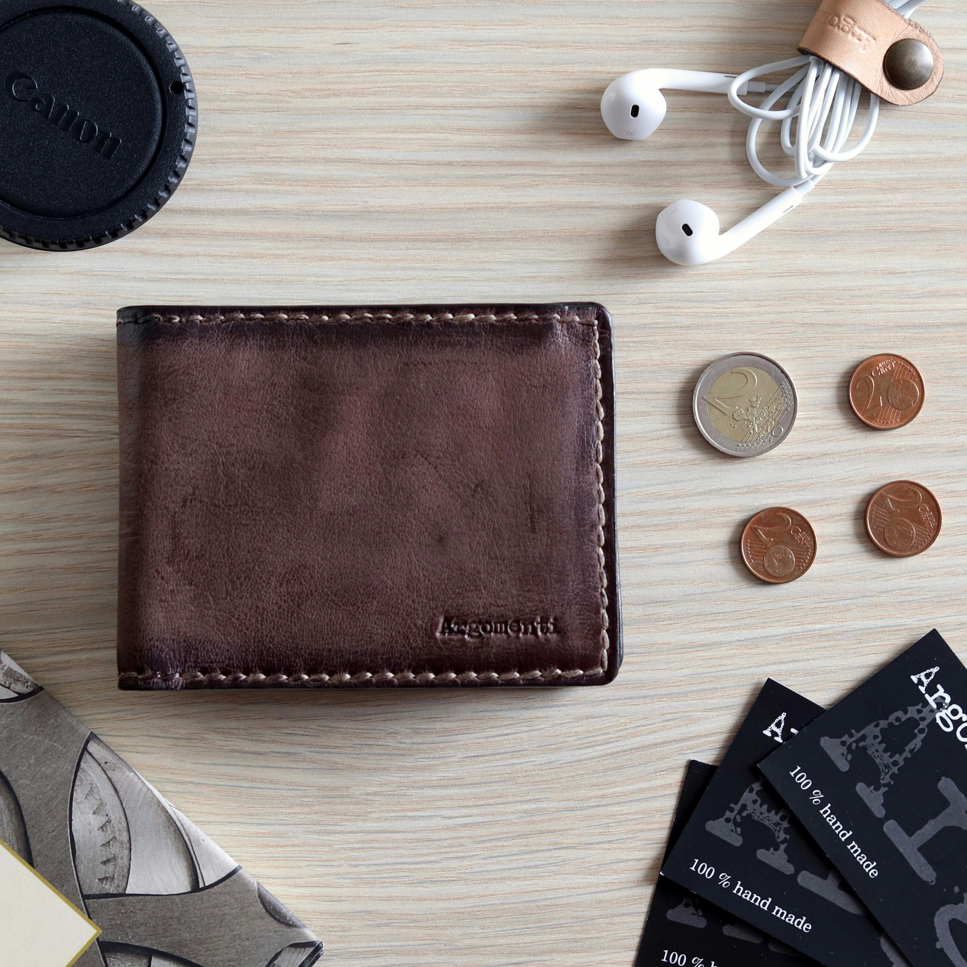 Cartera plegable de cuero marrón junto a monedas redondas de plata y estuche redondo negro