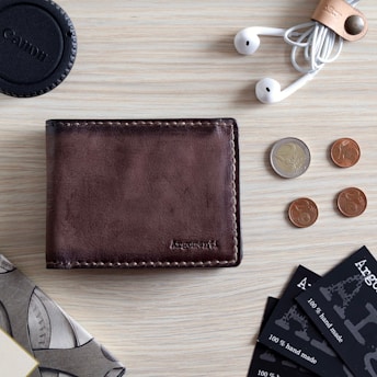 brown leather bifold wallet beside silver round coins and black round case