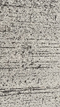 A close-up view of textured concrete with visible lines and small pebbles embedded in the surface.