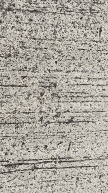 A close-up view of textured concrete with visible lines and small pebbles embedded in the surface.