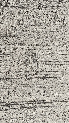 A close-up view of textured concrete with visible lines and small pebbles embedded in the surface.