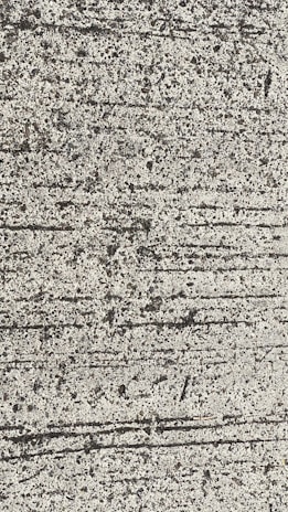A close-up view of textured concrete with visible lines and small pebbles embedded in the surface.