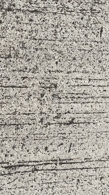 A close-up view of textured concrete with visible lines and small pebbles embedded in the surface.