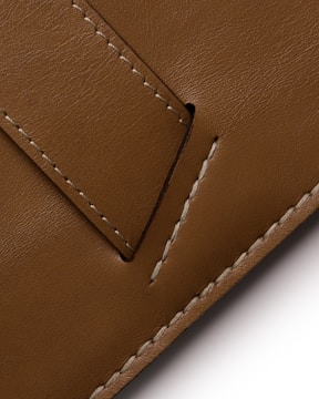 Detailed image features a close-up of brown leather material with visible stitching. The texture is smooth, and the stitches are white and prominent against the brown background, creating a contrast.