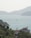 A peaceful coastal scene with a large villa in the foreground, surrounded by lush greenery. In the background, the calm sea stretches out towards a range of gently sloping hills. Several small boats are scattered across the water, contributing to the serene atmosphere.