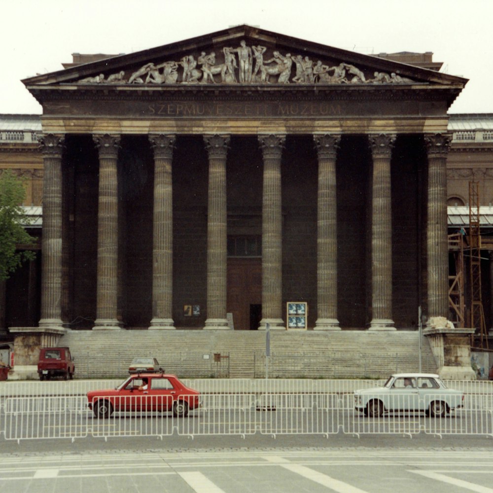 red car parked in front of gray concrete building during daytime