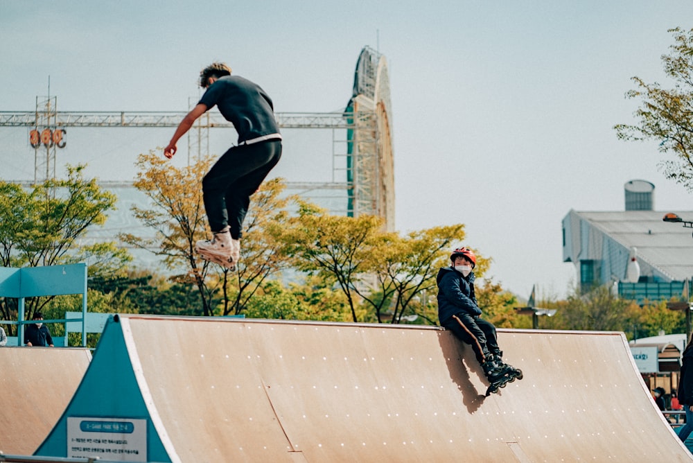 Mann in schwarzem Hemd und schwarzer Hose, der tagsüber auf blau-weißes Skateboard springt