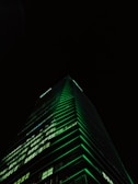 Luxurious modern skyscraper with deep navy and emerald lighting at dusk.
