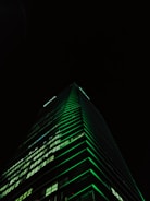 Luxurious modern skyscraper with emerald green lighting at dusk.