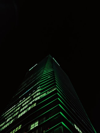 Luxurious modern skyscraper with deep navy and emerald lighting at dusk.