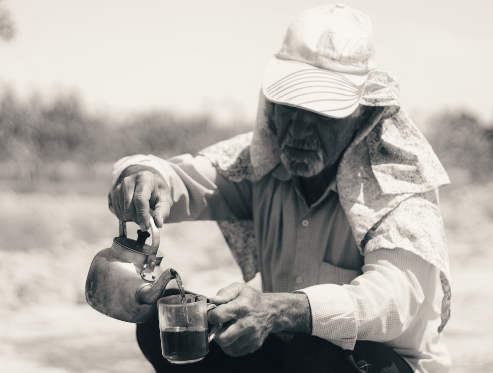 grayscale photo of man in jacket holding glass mug