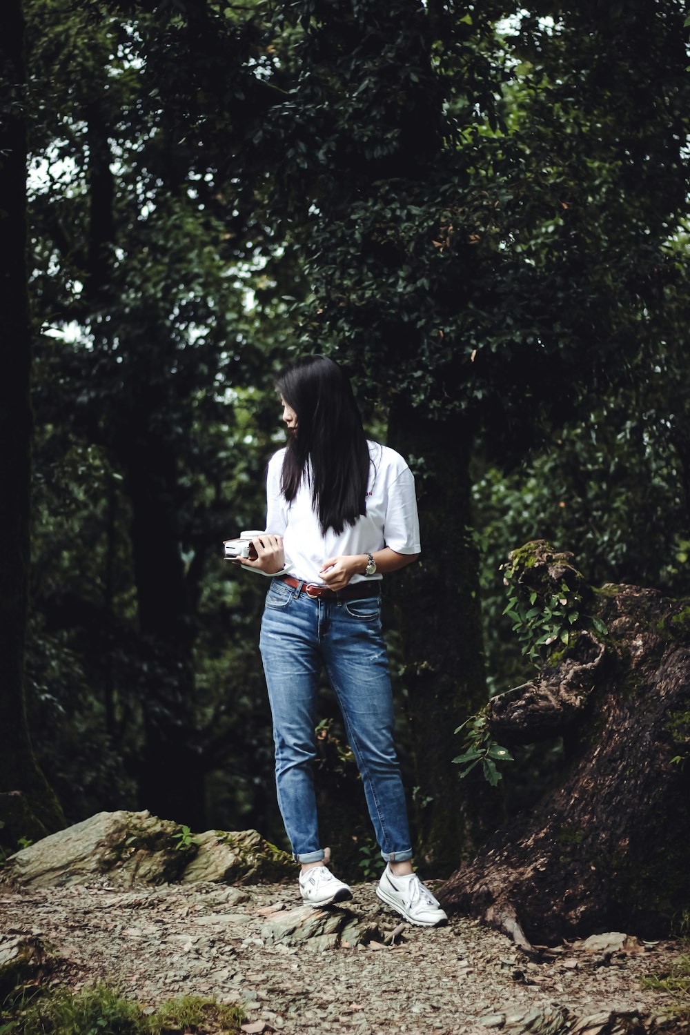 woman in white shirt and blue denim jeans standing on brown rock