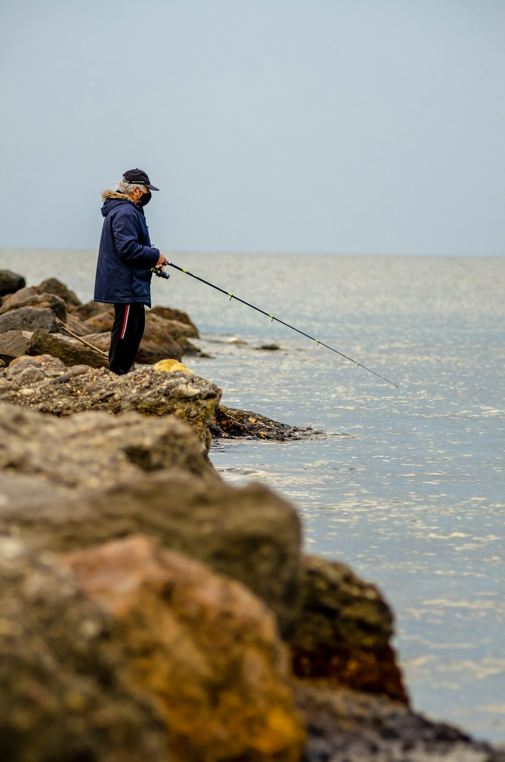 man in blue jacket and black pants fishing on sea during daytime