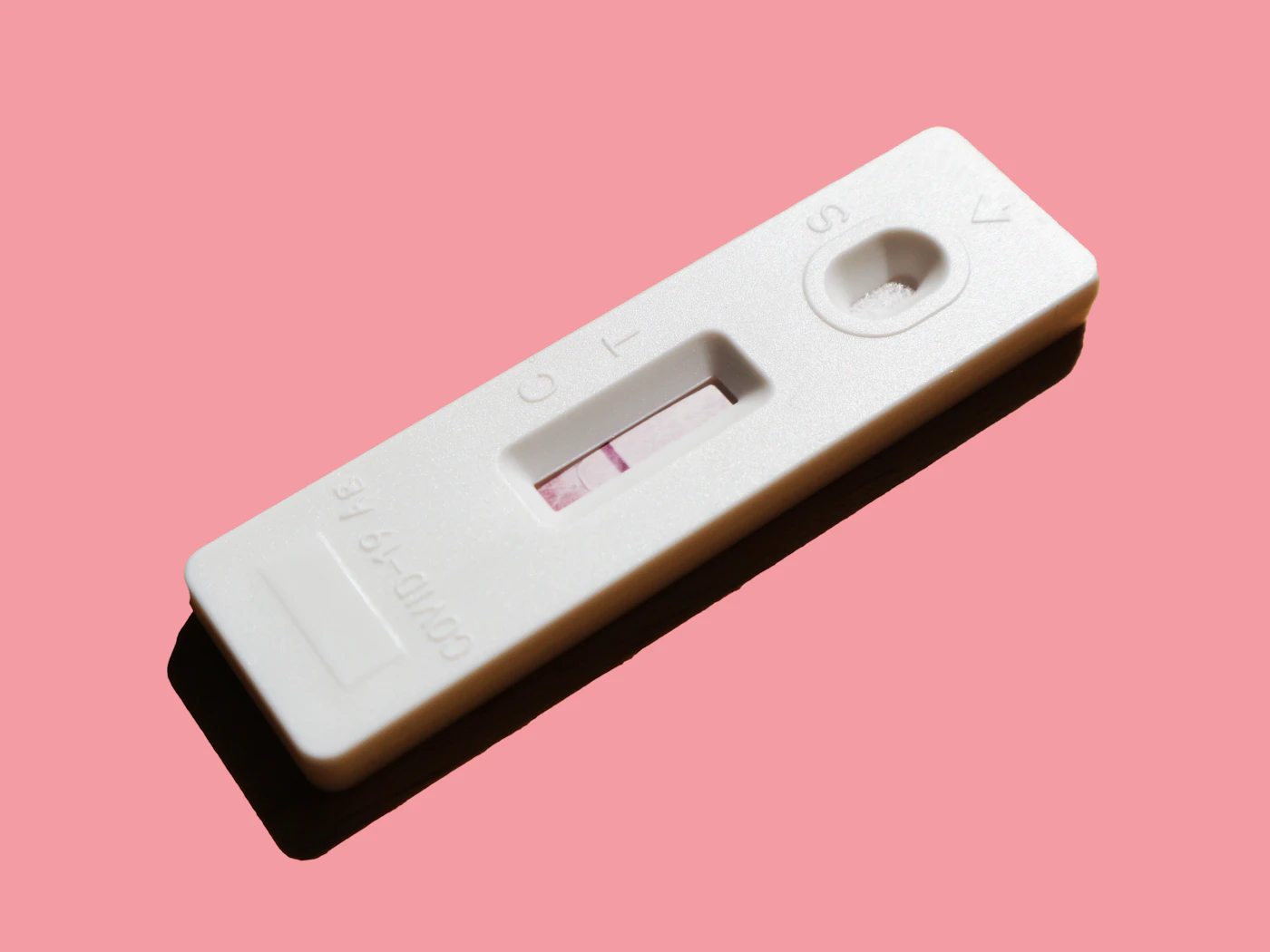 Teste de gravidez branco sobre fundo rosa claro — a espera de quem tenta engravidar com SOP