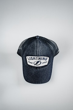 A black baseball cap with a mesh back and a front patch displaying the word 'LIGHTNING' with the text 'Estab. 1992' underneath. The cap is positioned on a flat, light-colored surface.