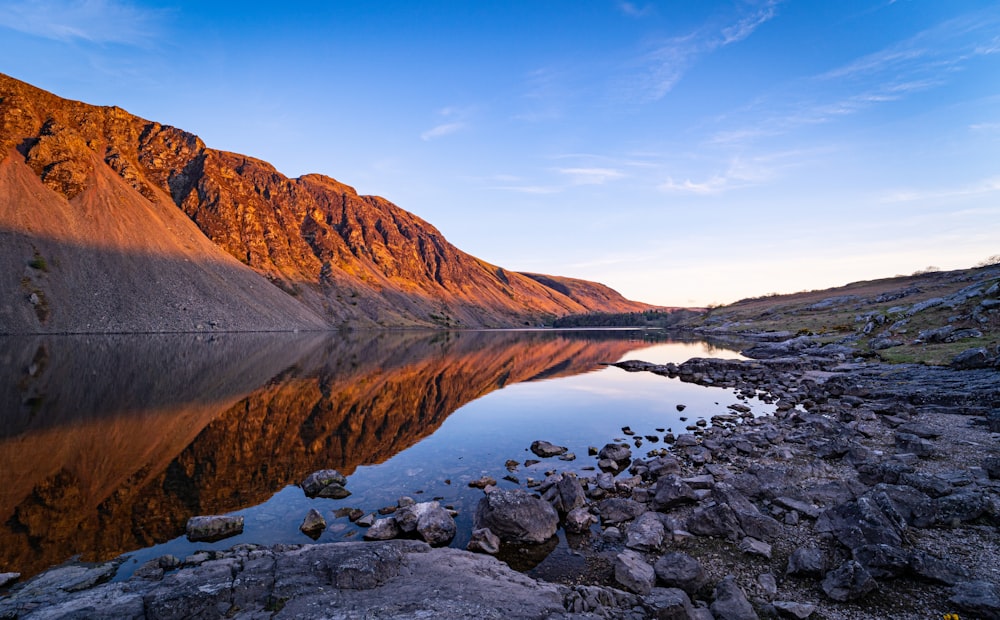 brown mountain near body of water under blue sky during daytime