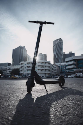 A sleek black electric scooter parked on a city sidewalk with a sunset backdrop