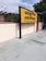 A yellow and black signboard prominently displays the name 'ABUROAD' in both Hindi and English, along with additional text in red below. The sign is positioned on a platform with a tiled floor. Greenery is visible in the background along with a blue sky partially covered by clouds.