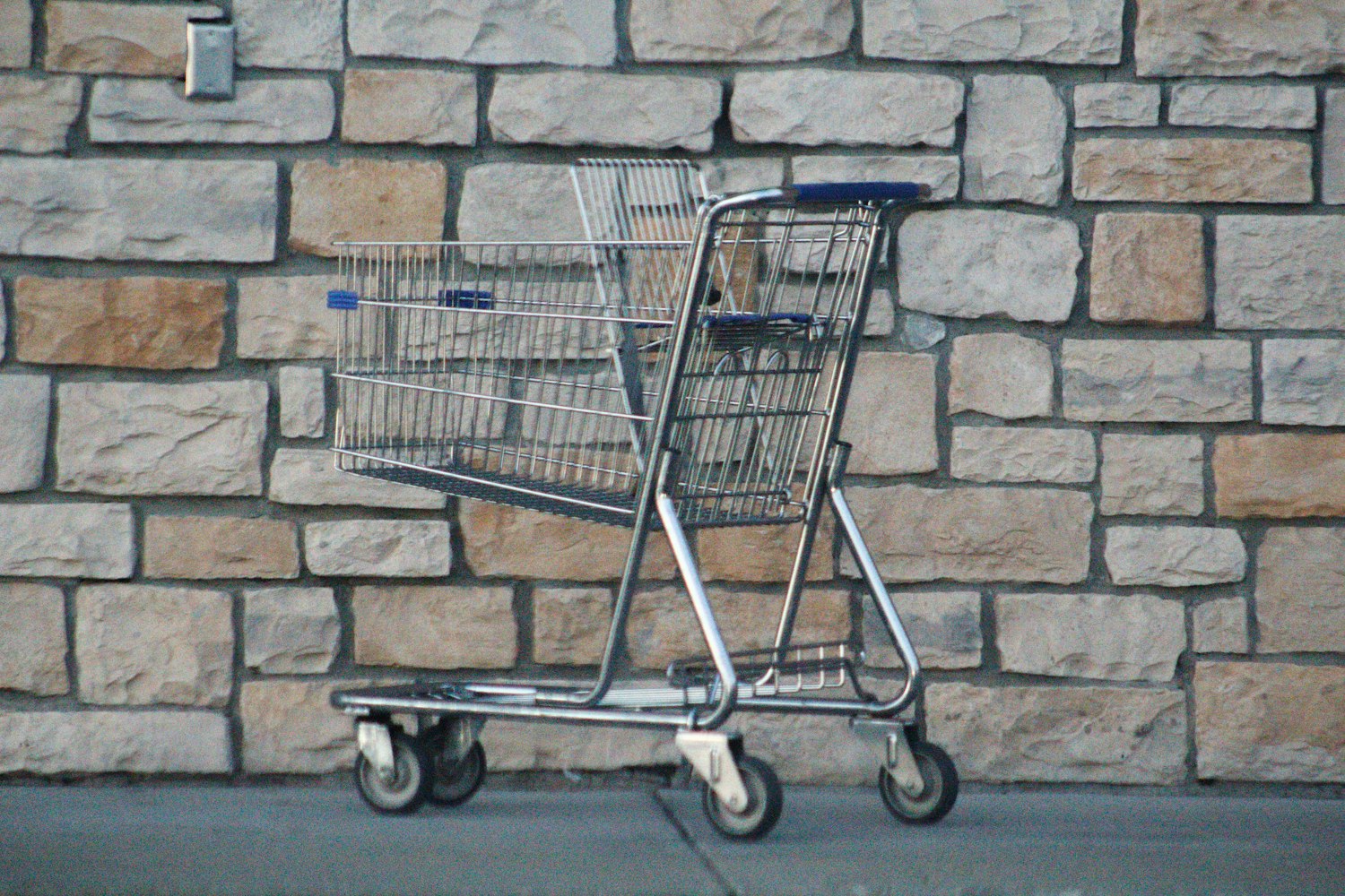 gray shopping cart on gray brick wall by Joshua Hoehne