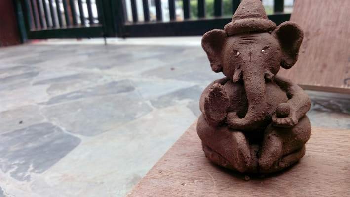 A serene wooden murti of Lord Ganesha with intricate carvings placed on a simple earthen shelf.