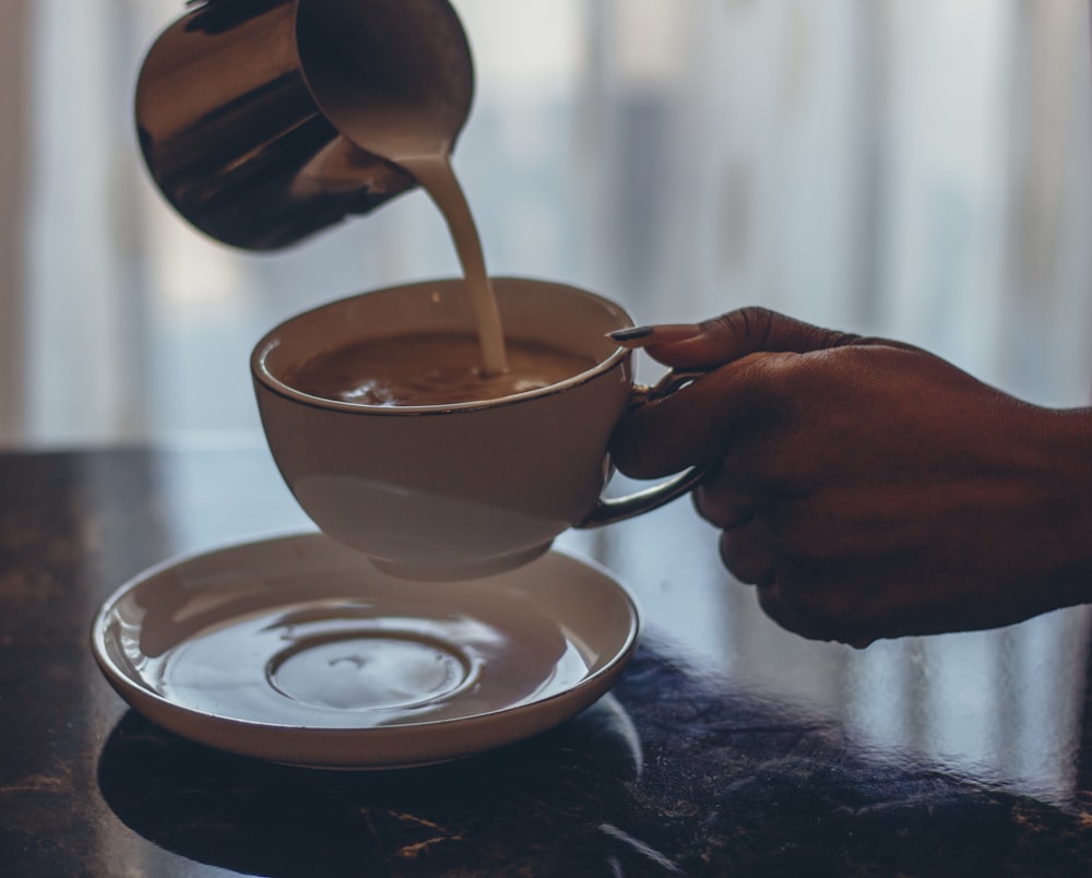 person holding white ceramic mug with brown wooden spoon