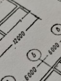 Close-up view of a technical drawing or blueprint featuring measurements and diagrams. The image shows lines, numbers, and symbols commonly used in architectural or engineering designs.