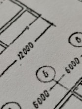 Close-up view of a technical drawing or blueprint featuring measurements and diagrams. The image shows lines, numbers, and symbols commonly used in architectural or engineering designs.