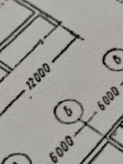 Close-up view of a technical drawing or blueprint featuring measurements and diagrams. The image shows lines, numbers, and symbols commonly used in architectural or engineering designs.